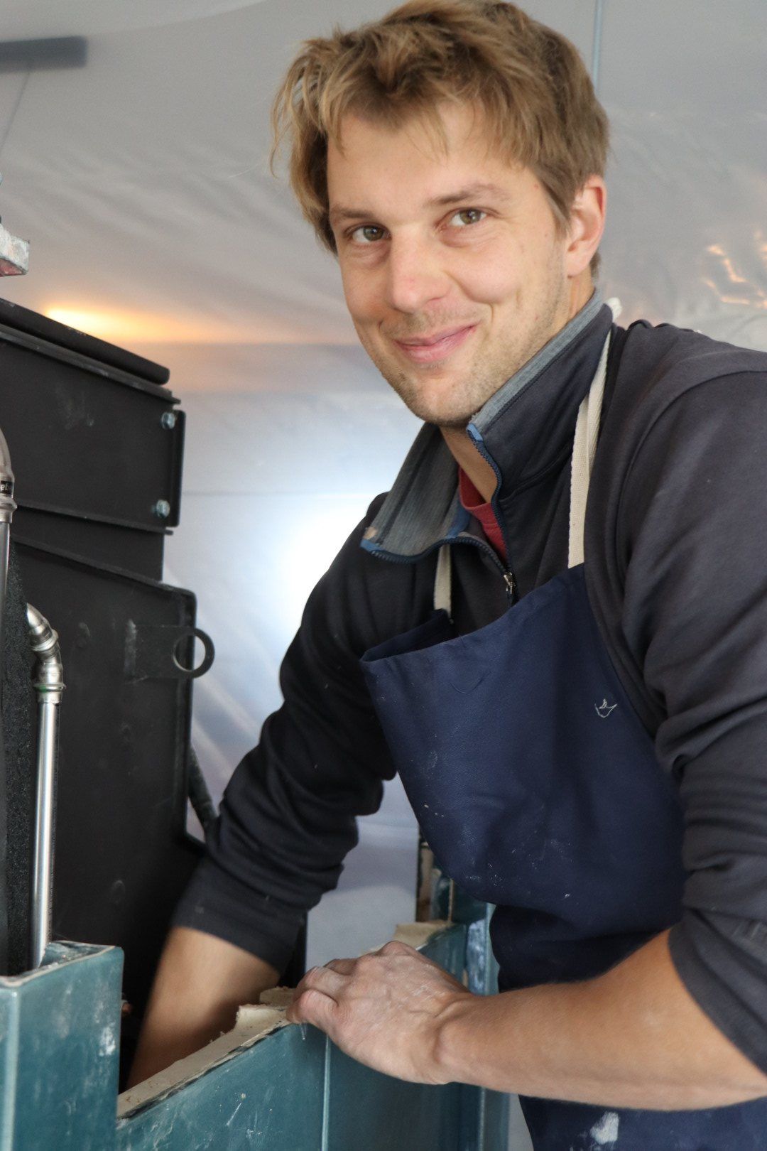 Ofenbaumeister Fiete Paul in Arbeitsschürze lächelt in die Kamera
