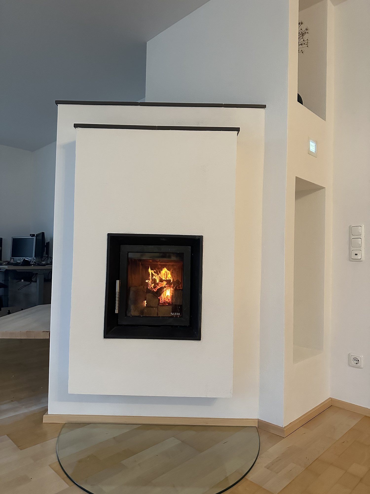 Schlichter weißer Kamin mit quadratischer Sichtscheibe und Feuer auf halbrunder Glasbodenplatte