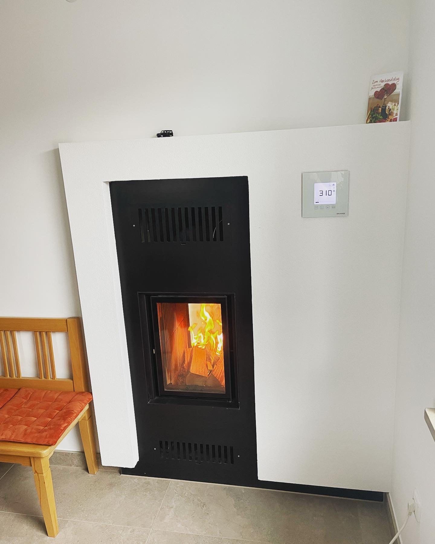 Wandkamin mit schwarzer Front, Lüftungsgittern und Feuer in einer weißen Wand